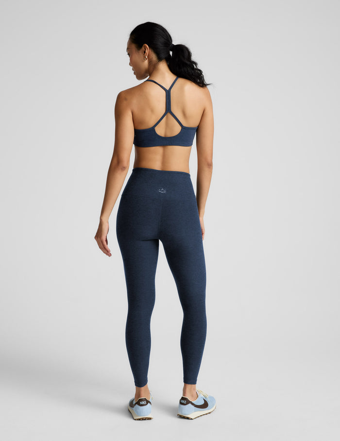 Woman wearing a navy blue sports bra and leggings set on a light gray background.