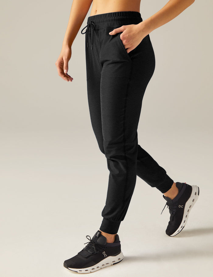 Side view of person walking in black Spacedye Commuter Midi Joggers with a drawstring waist, pockets, and banded cuffs.