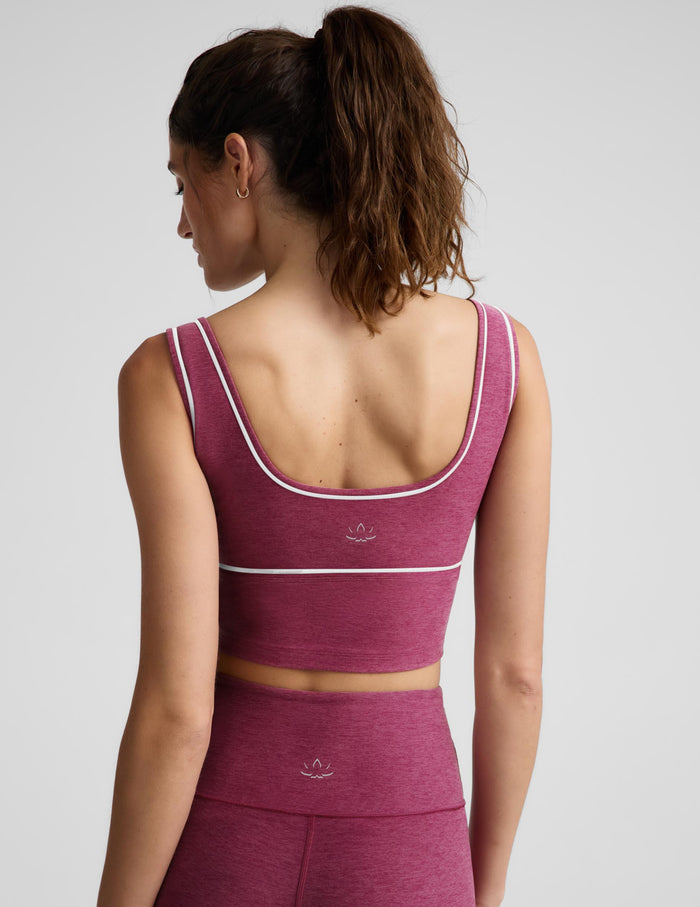 A woman modeling a matching athletic set consisting of a heathered magenta crop top and leggings with thin white contrast piping, photographed against a light gray studio background.