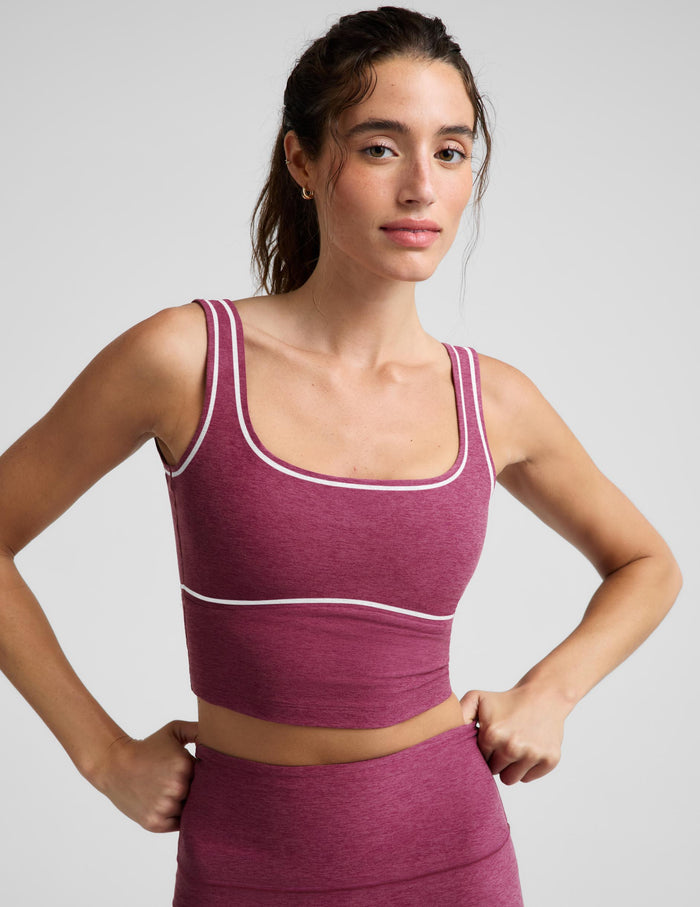 A woman modeling a matching athletic set consisting of a heathered magenta crop top and leggings with thin white contrast piping, photographed against a light gray studio background.