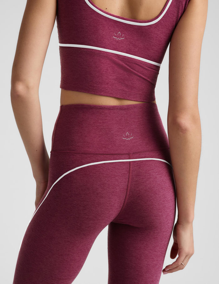 A close-up of a model wearing a matching heathered burgundy activewear set with white contrast piping and a small white Adidas logo on the sports bra and leggings.