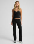 A woman modeling a black ribbed tank top and matching black wide-leg pants with a foldover waistband against a light gray studio background.