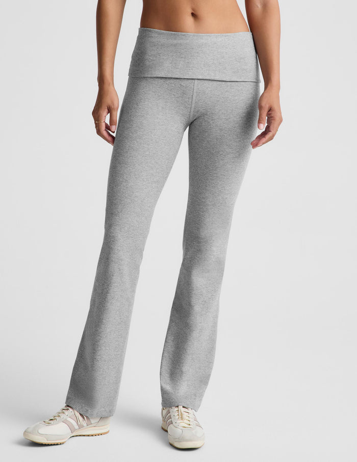 A woman modeling a light gray two-piece activewear set consisting of a sports bra and high-waisted bootcut leggings, standing against a light gray studio background.