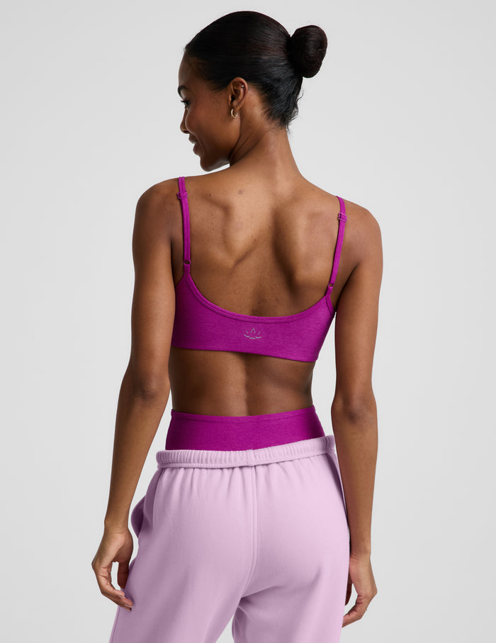 Woman wearing a purple bra and sweatpants against a plain background.