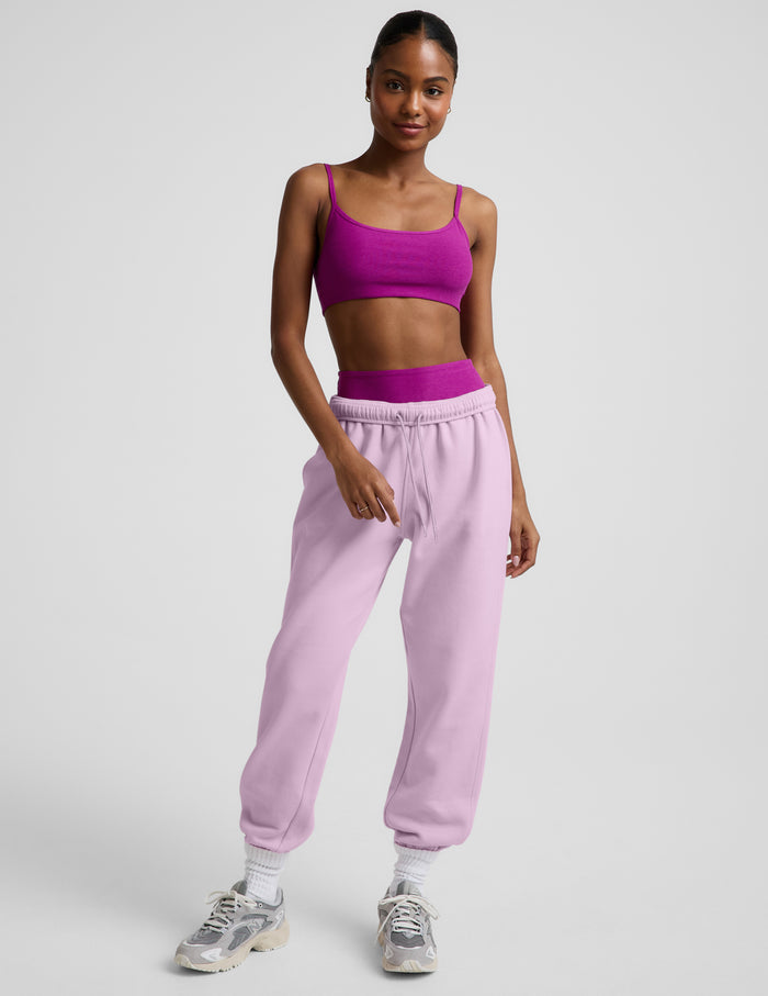 Woman wearing a purple bra and sweatpants against a plain background.