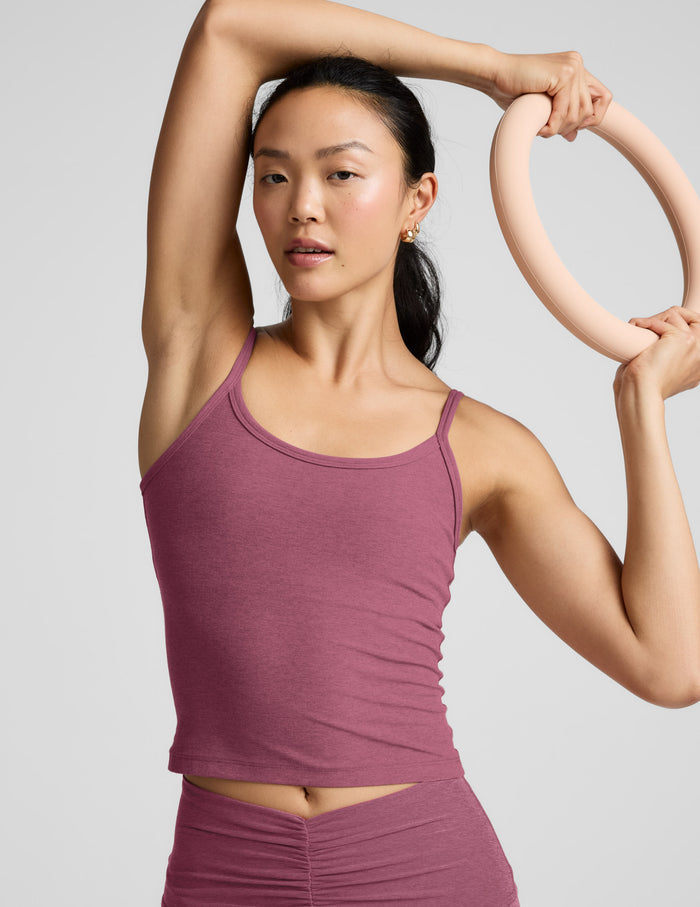 Woman wearing a purple waist length tank and leggings against a plain background.