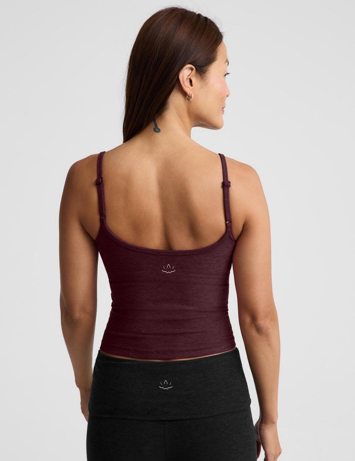 A woman modeling a dark burgundy spaghetti-strap tank top and black pants against a light gray studio background.