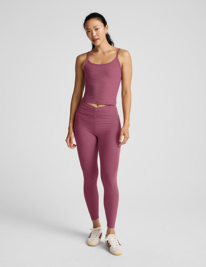 Woman wearing a purple waist length tank and leggings against a plain background.