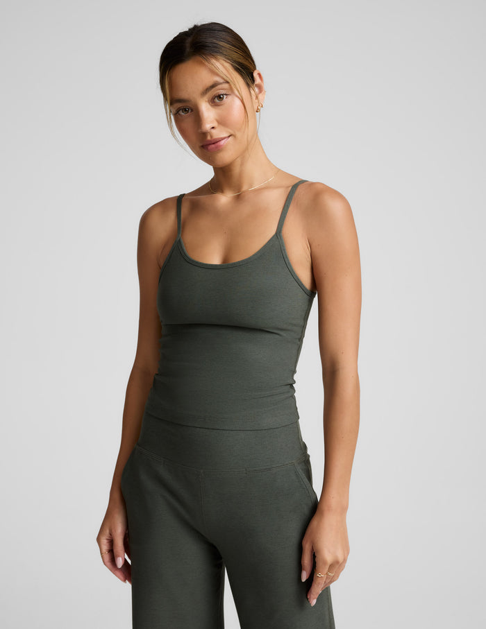 Woman wearing a green waist length tank and pants against a plain background.