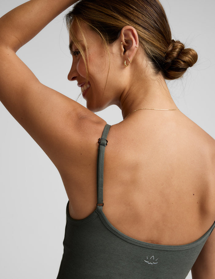 Woman wearing a green waist length tank and pants against a plain background.