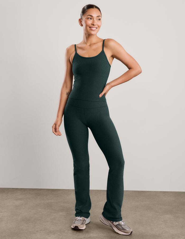 A woman modeling a dark forest green athletic tank top and matching high-waisted pants against a light gray studio background.