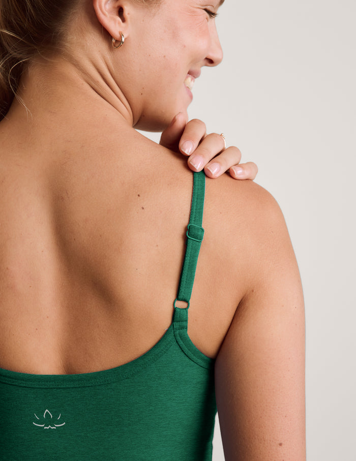 Woman wearing a green waist length tank and green sweatpants against a plain studio background.