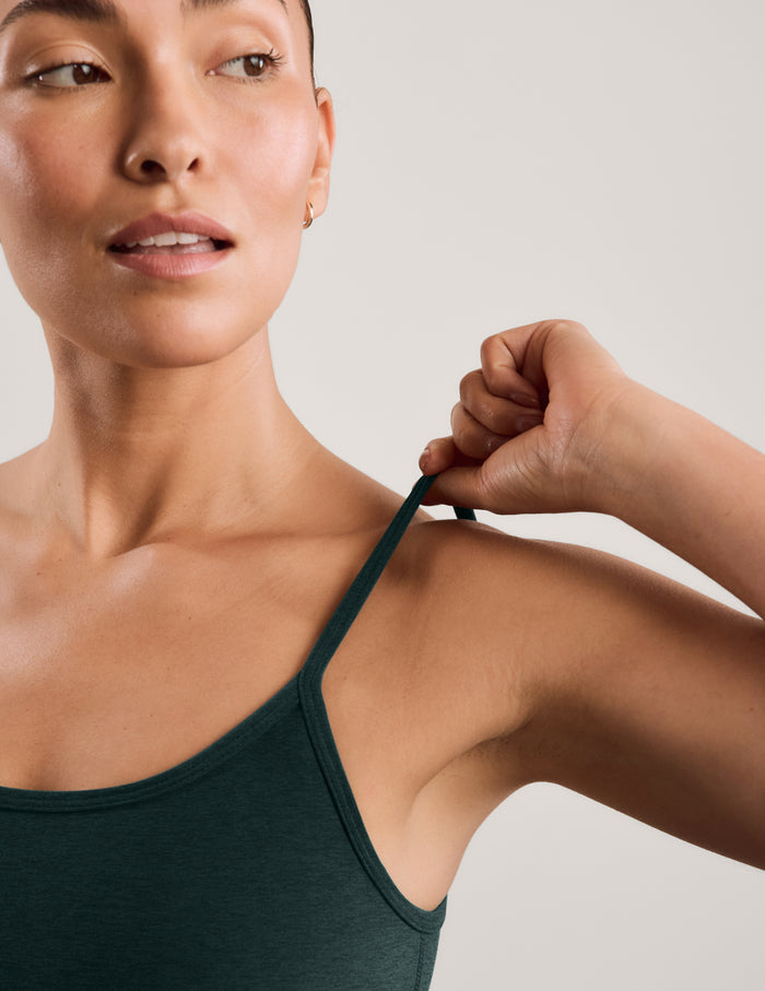 A woman modeling a dark forest green athletic tank top and matching high-waisted pants against a light gray studio background.