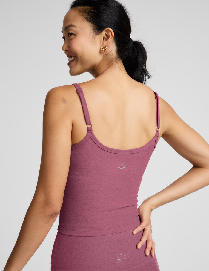 Woman wearing a purple waist length tank and leggings against a plain background.