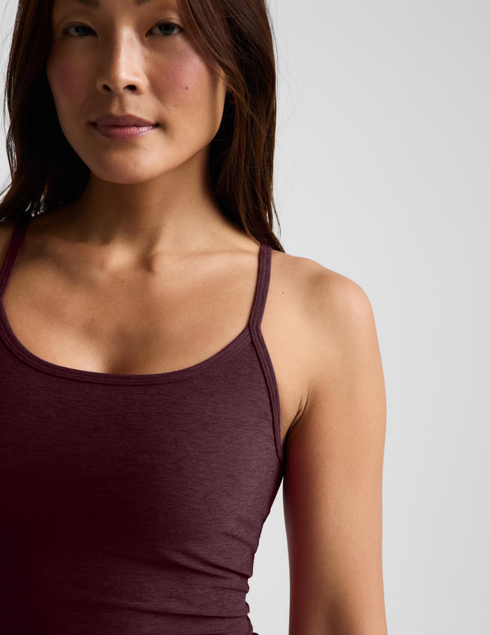 A woman modeling a dark burgundy spaghetti-strap tank top and black pants against a light gray studio background.