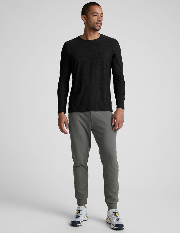 A man models the dark grey Spacedye Freefit Men's Zipper Pockets Jogger with a black long-sleeve shirt and white sneakers.