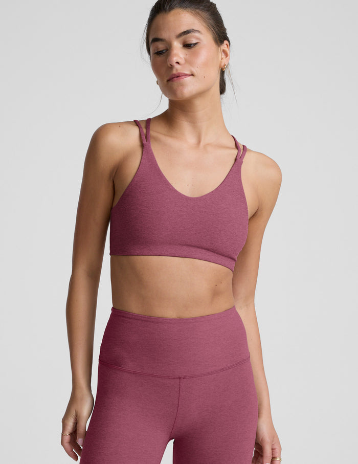 Woman wearing a purple sports bra and and leggings on a light gray background.