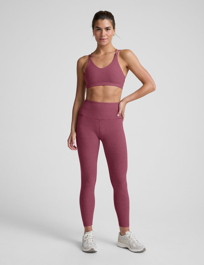 Woman wearing a purple sports bra and and leggings on a light gray background.