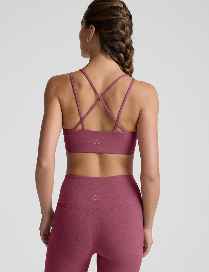 Woman wearing a purple sports bra and and leggings on a light gray background.
