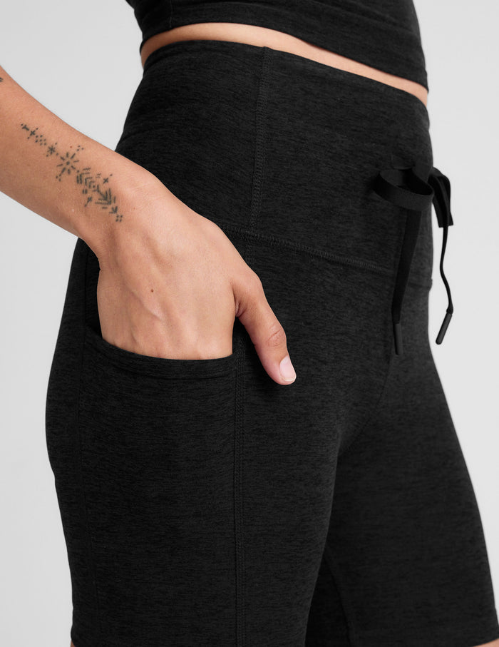 Close-up of black Spacedye Go Pocket 5" Short showing the high waistband, drawstring detail, and a hand in the side pocket.