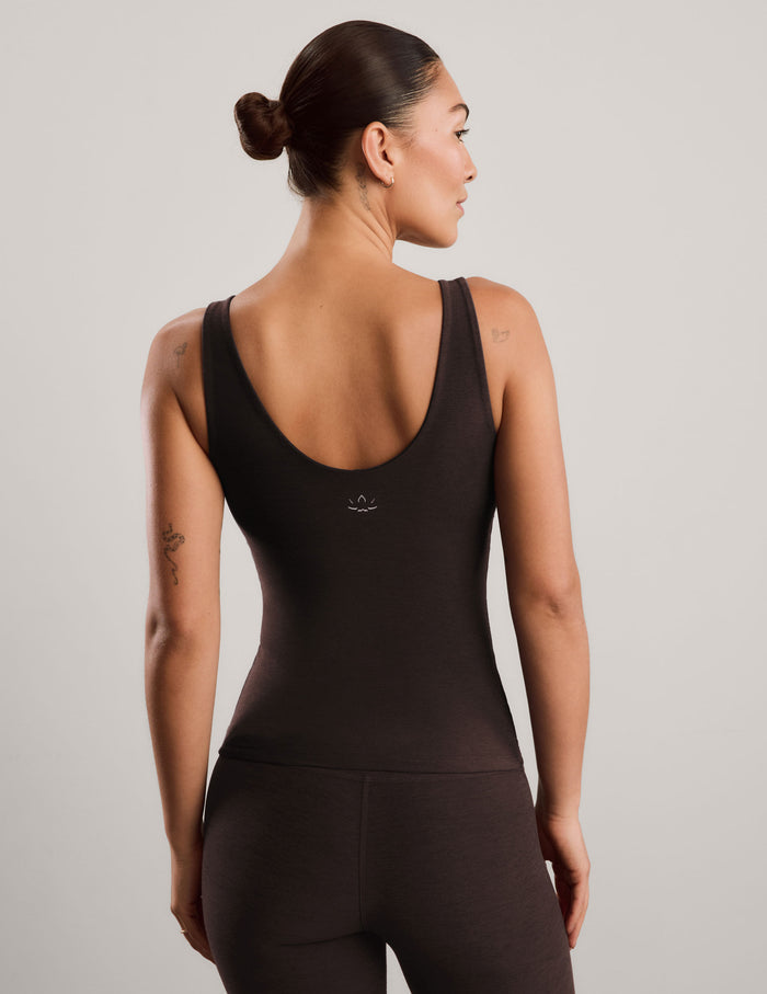 A woman modeling a dark brown v-neck tank top and matching leggings against a light gray studio background.