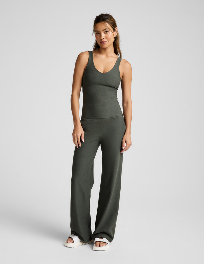Woman wearing a full length green v-neck tank and pants against a plain background.