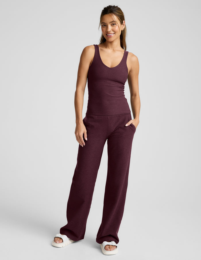 A woman modeling a matching two-piece active set in a deep red color, consisting of a sleeveless scoop-neck tank top and wide-leg pants, photographed against a neutral light gray background.