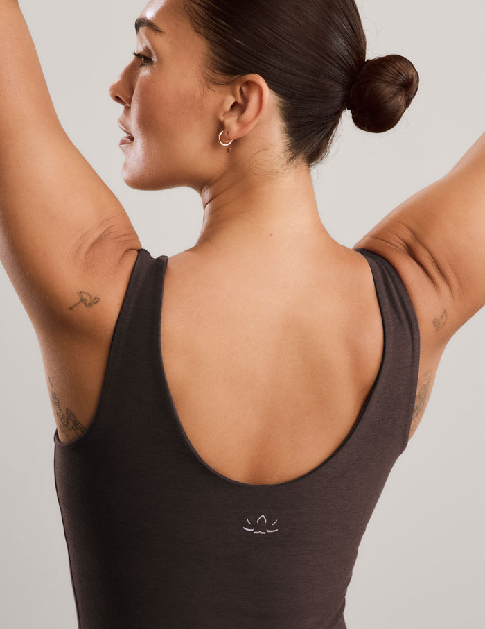 A woman modeling a dark brown v-neck tank top and matching leggings against a light gray studio background.