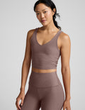 Woman wearing a brown v-neck cropped tank and leggings against a gray background.