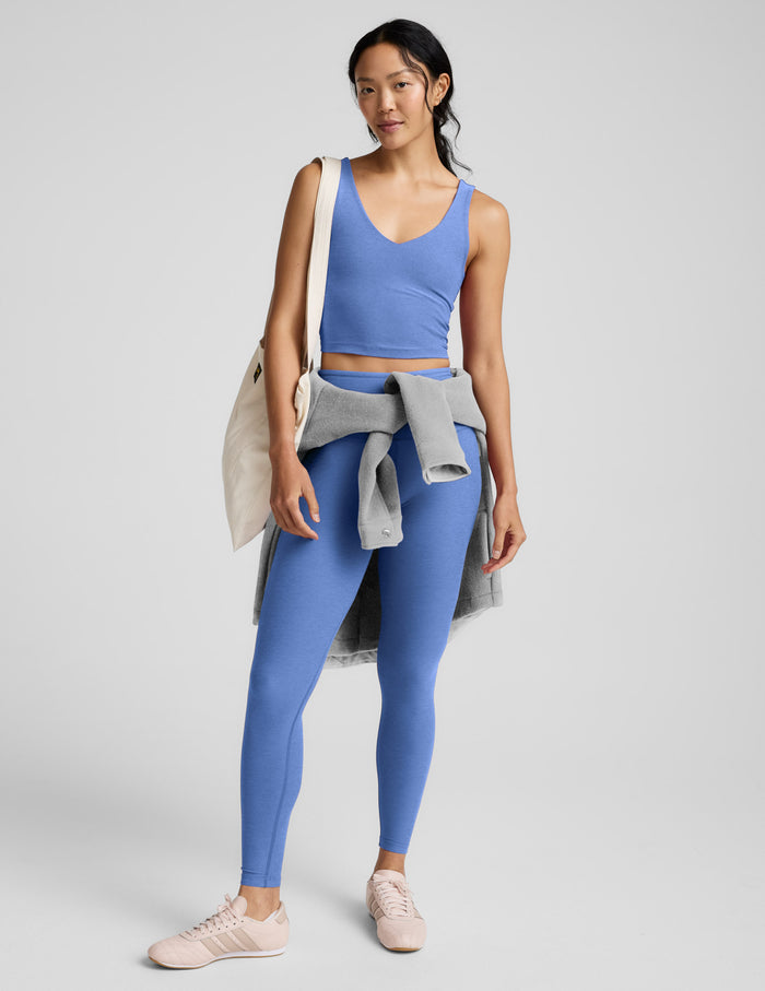 Woman wearing a blue cropped v-neck tank and leggings against a plain background.