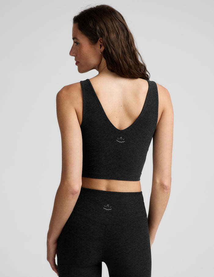 A woman modeling a black scoop-neck athletic crop top and matching black leggings against a light gray studio background.