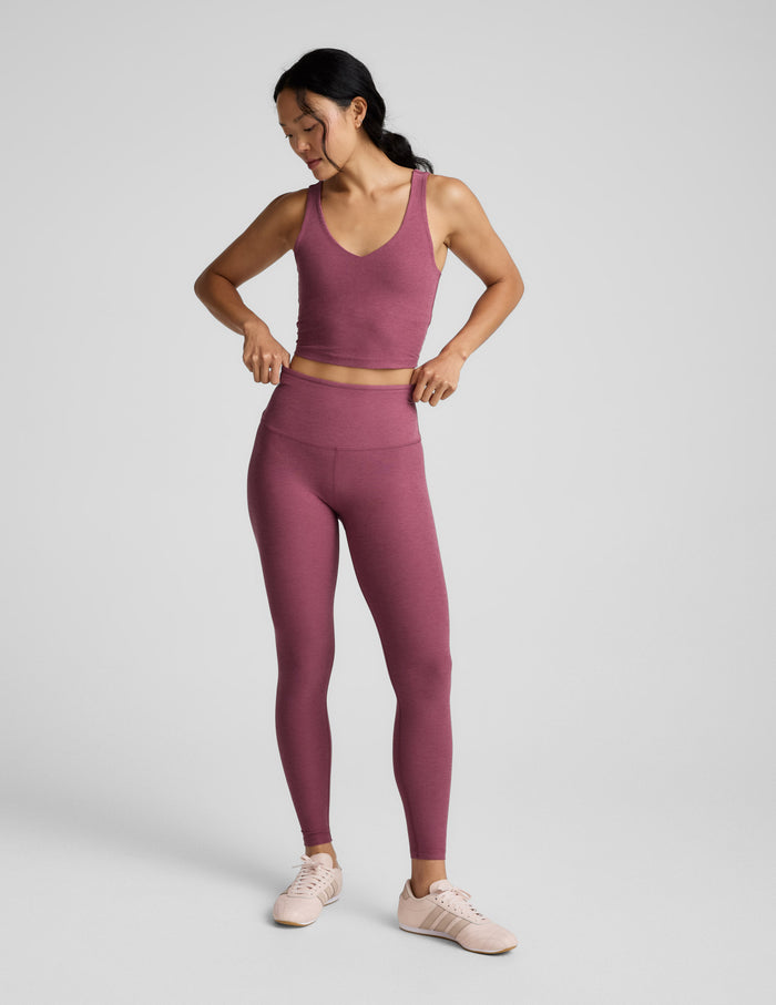 Woman wearing a v-neck cropped tank and leggings against a plain background.