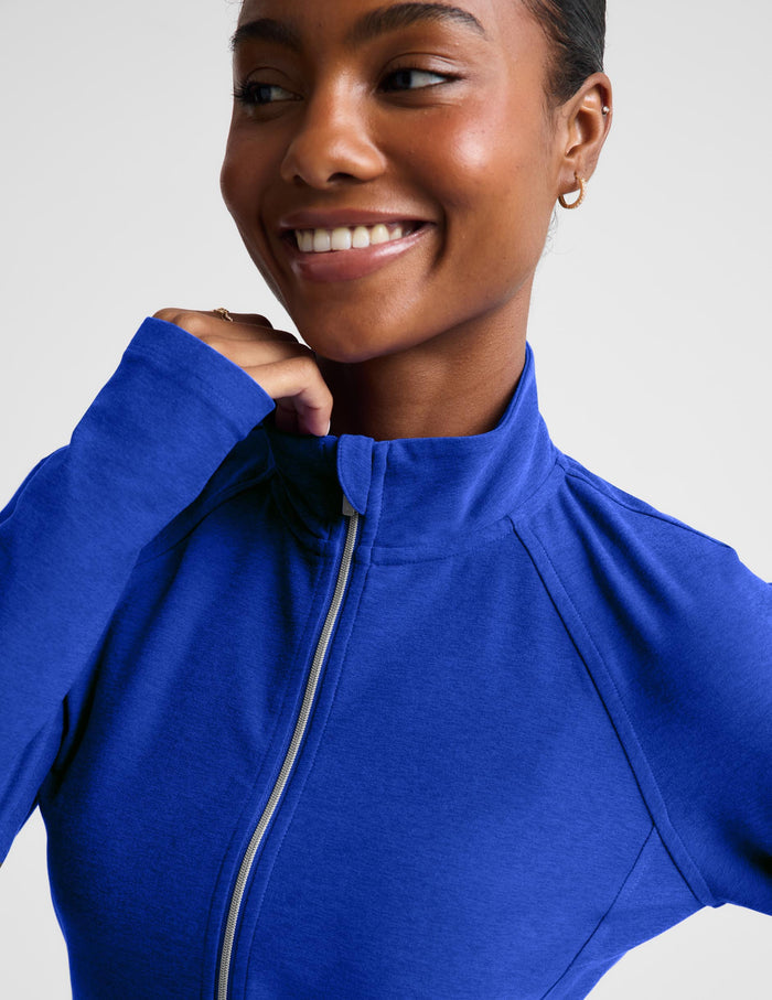 A model wearing a royal blue long-sleeve athletic zip-up top and matching high-waisted shorts against a light gray studio background.