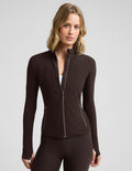 Woman wearing a brown full length zip-up jacket and brown leggings against a plain background.