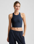 Woman wearing a blue high-neck cropped racerback tank and blue joggers against a plain background.