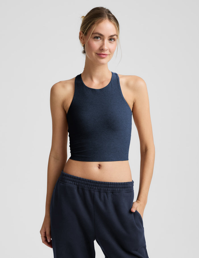 Woman wearing a blue high-neck cropped racerback tank and blue joggers against a plain background.