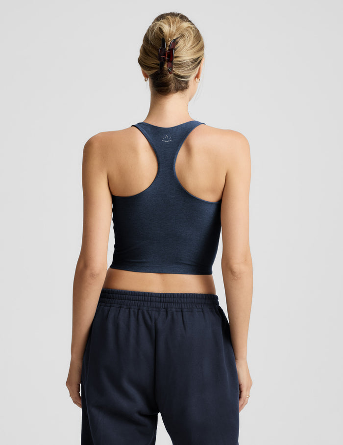 Woman wearing a blue high-neck cropped racerback tank and blue joggers against a plain background.