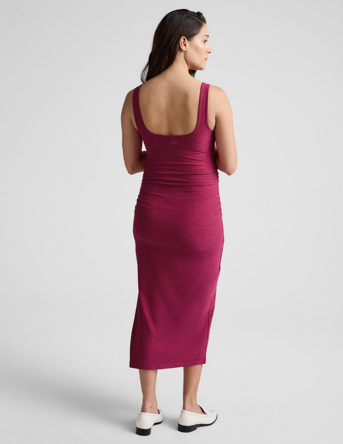Woman wearing a magenta maternity midi length dress against a plain background.