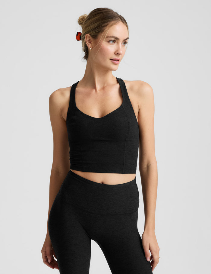 Woman wearing a black v-neck cropped racerback tank and leggings on a light gray background.