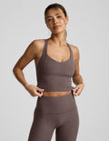 Woman wearing a brown v-neck racerback cropped tank and leggings on a light gray background.