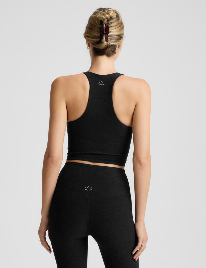 Woman wearing a black v-neck cropped racerback tank and leggings on a light gray background.