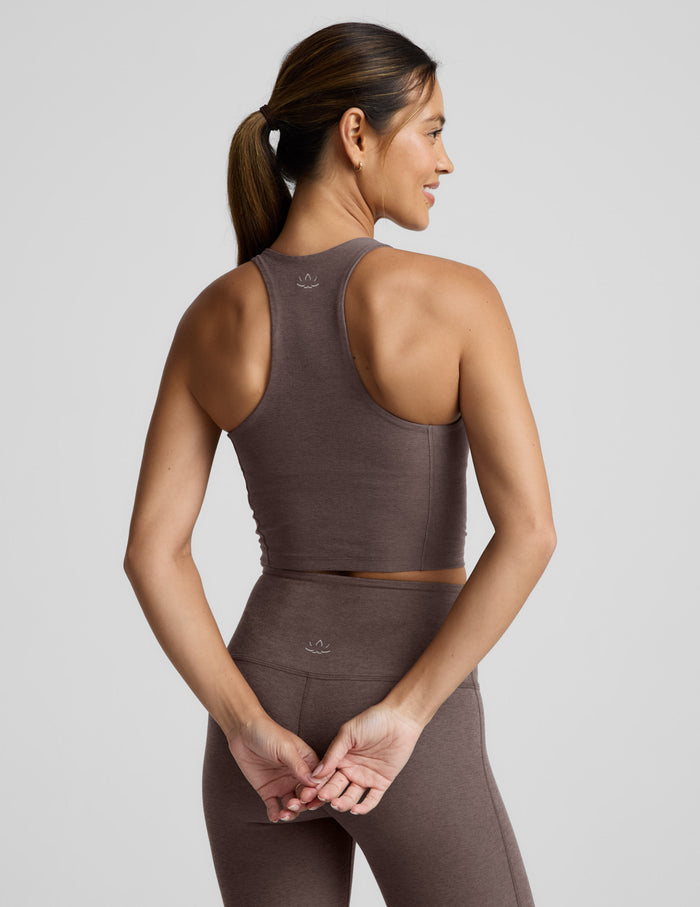 Woman wearing a brown v-neck racerback cropped tank and leggings on a light gray background.