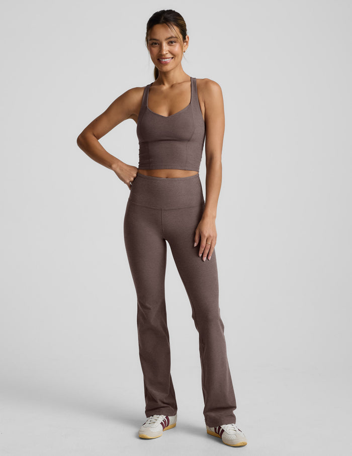 Woman wearing a brown v-neck racerback cropped tank and leggings on a light gray background.