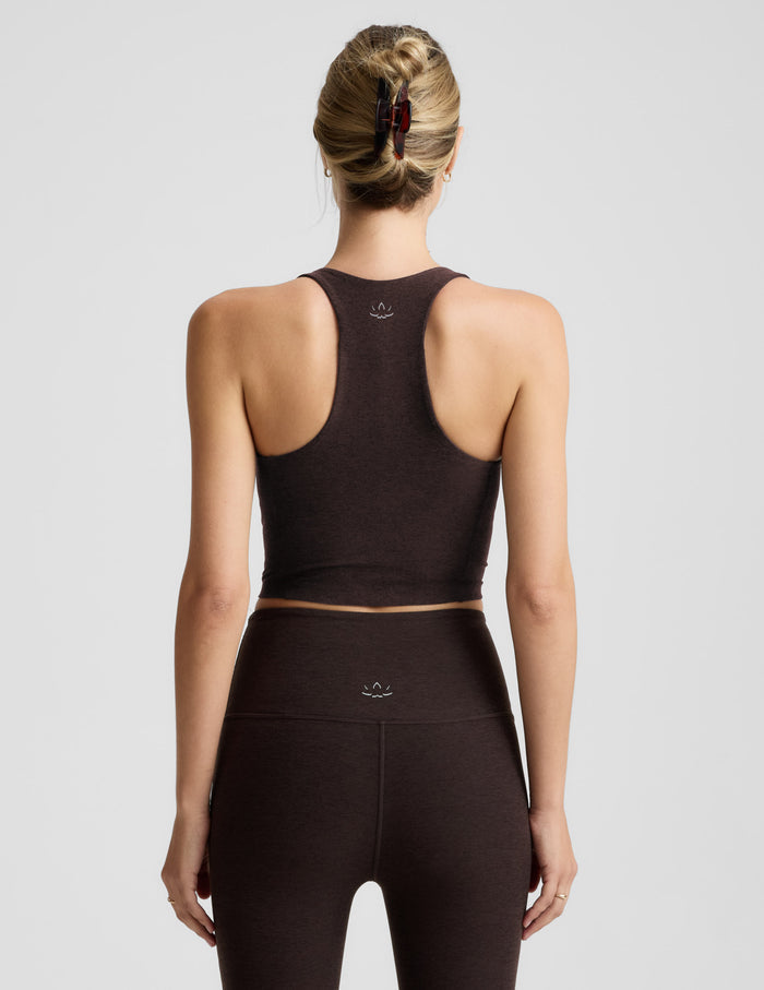 Woman wearing a brown v-neck racerback cropped tank and leggings on a light gray background.