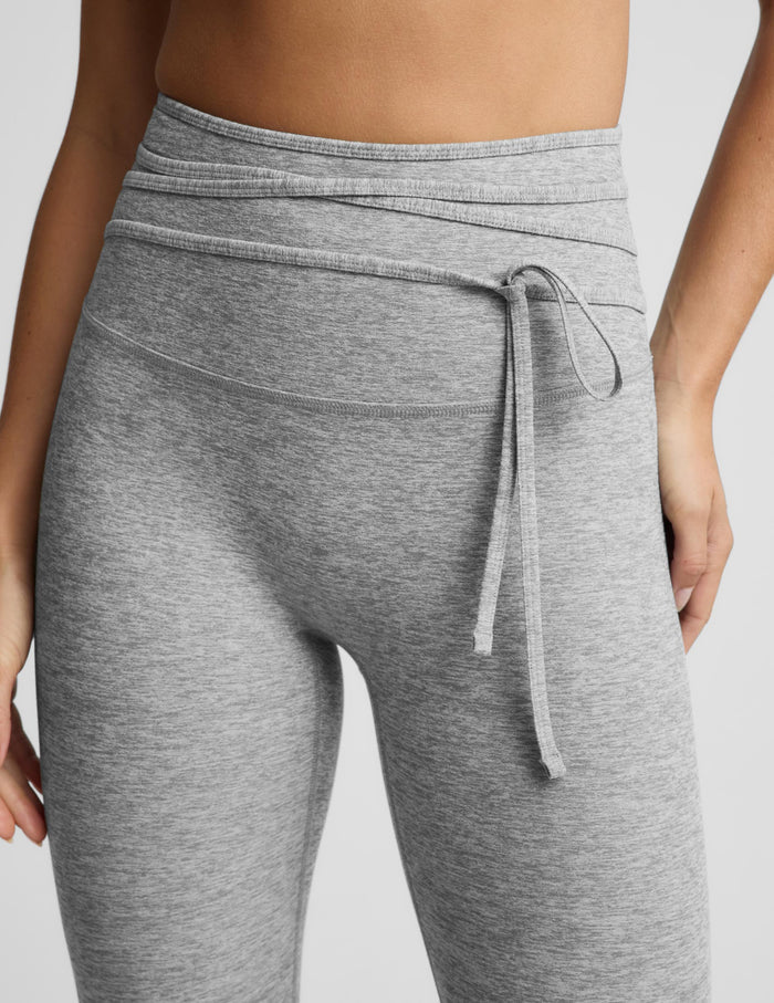Close-up of a model wearing heather gray high-waisted leggings with a drawstring waistband, shown from the waist to mid-thigh against a light gray studio background.
