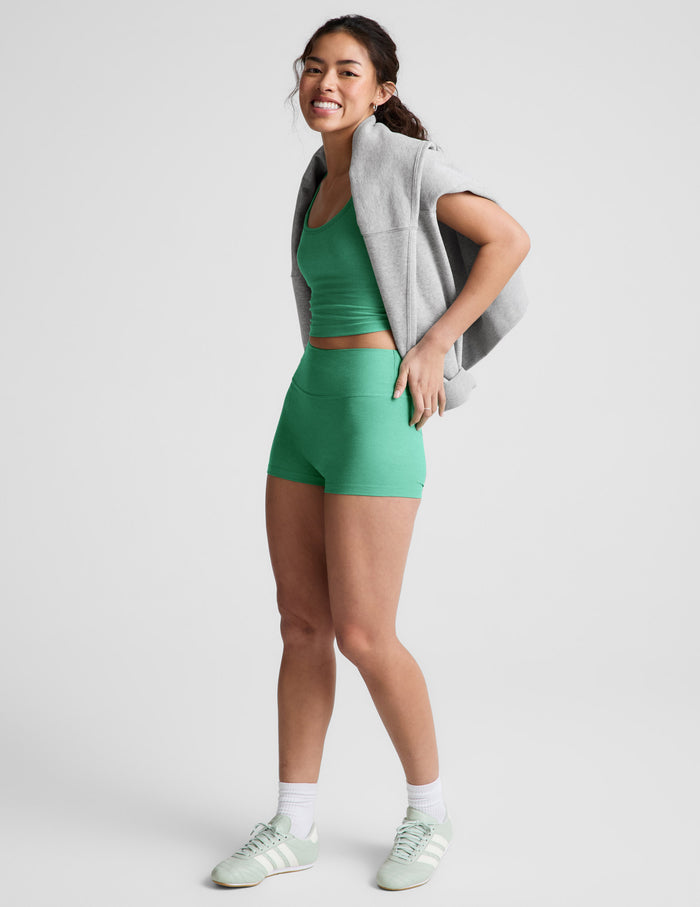 Smiling woman wears green Spacedye Keep Pace 3" Mid-Rise Short, matching tank, and a grey sweatshirt over her shoulders.