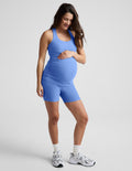 Spacedye Keep Pace 5" Maternity Pocket Biker Short in blue, worn by a pregnant person with a matching tank and sneakers.