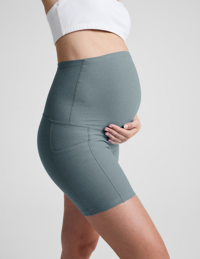 Side profile of woman wearing green Spacedye™ Keep Pace 5" Maternity Pocket Biker Short with a white top and side pockets.