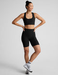 Woman wearing a black sports bra and biker shorts on a light gray background
