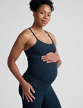 Pregnant woman wearing a dark blue tank top and leggings on a light gray background.